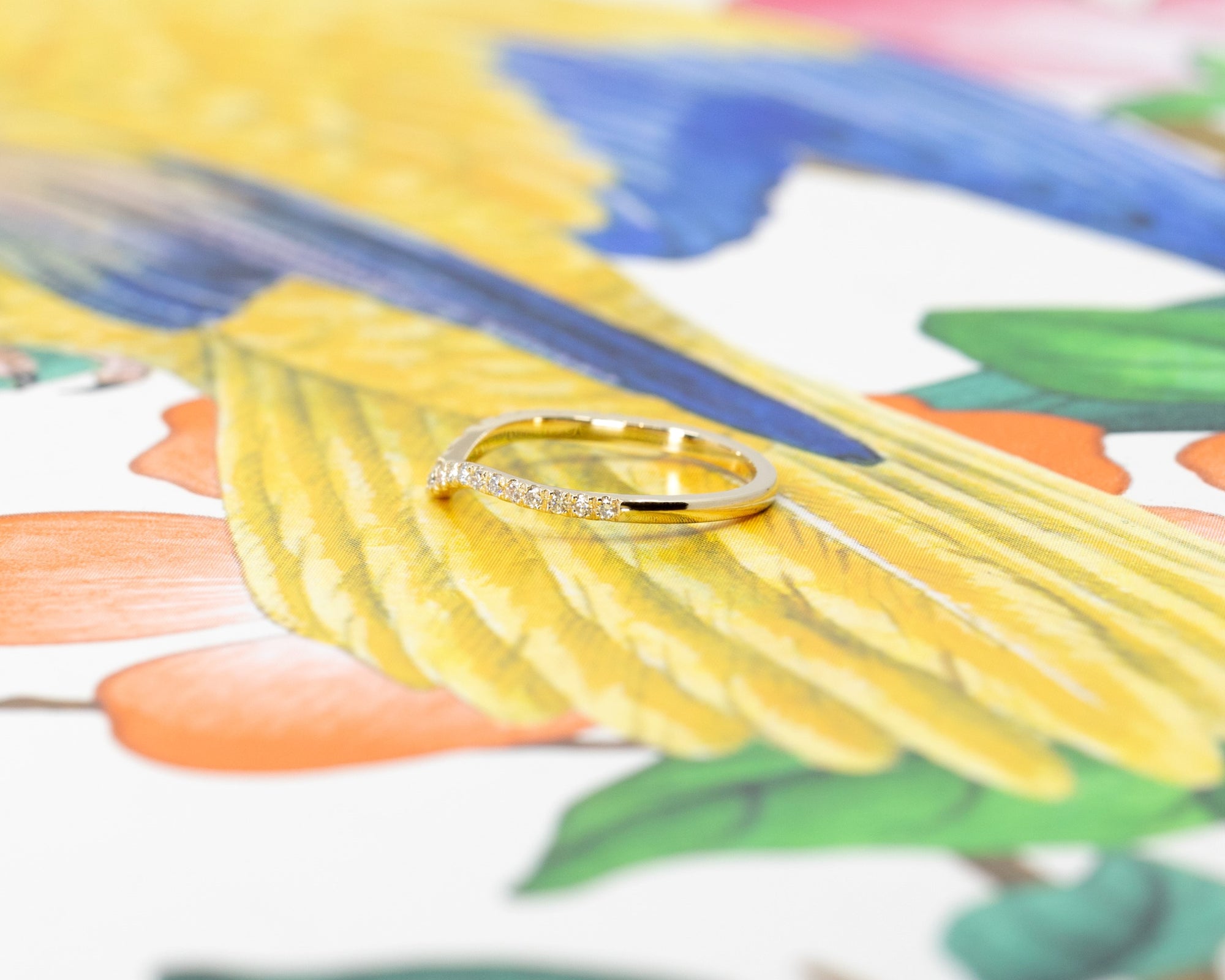 Elegant yellow gold wedding band with a gentle curve and sparkling diamonds, shown on a vibrant background. Designed by Bena Jewelry in Montreal.