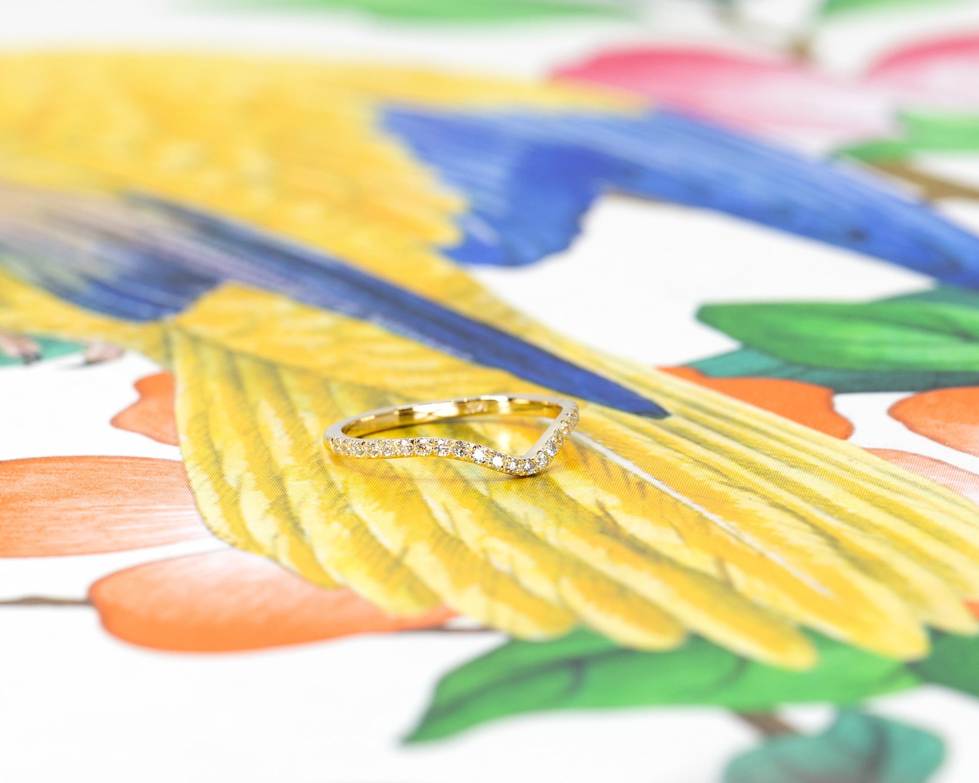 Custom bridal wedding band in yellow gold with a curved design and diamonds, displayed on a soft-colored backdrop. Made by Bena Jewelry, Montreal, Canada.