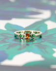 Modern yellow gold ring with vibrant orange and green gemstones, photographed against a warm-colored background. Custom-made by Bena Jewelry in Montreal.