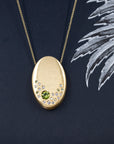 Close-up of the handcrafted gold pendant by Bena Jewelry – Featuring a soft brushed finish, this unique design highlights vibrant green peridots and sparkling diamonds.