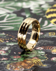 Bena Jewelry presents Trois Vagues yellow gold men's wedding band with three central lines, shown against a dark-colored background.