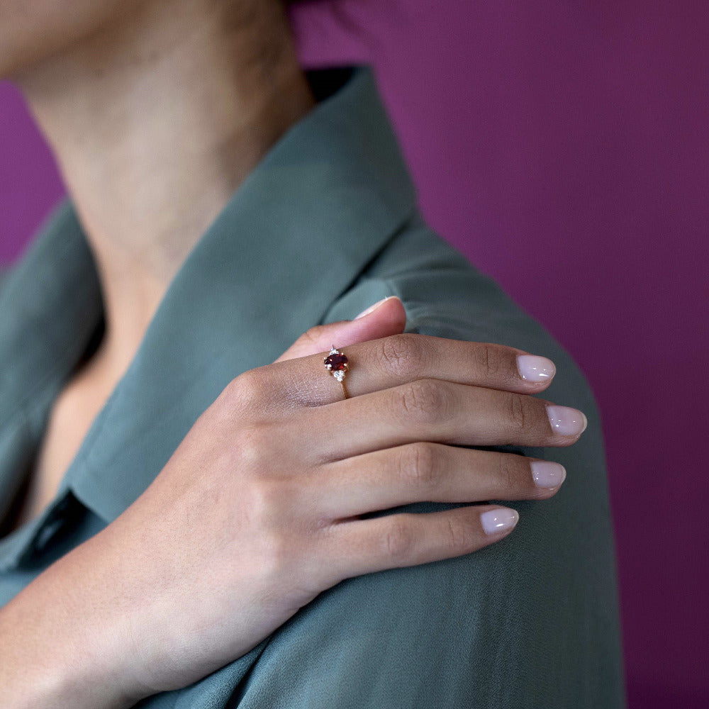 Yellow gold Désir Pyrope Garnet Ring with an oval garnet and side diamonds worn by a woman resting her hand on her shoulder elegant bridal jewelry by Bena Jewelry custom-made in Montreal
