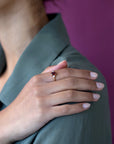 Yellow gold Désir Pyrope Garnet Ring with an oval garnet and side diamonds worn by a woman resting her hand on her shoulder elegant bridal jewelry by Bena Jewelry custom-made in Montreal