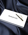 Product photo of a solid yellow gold fashion ring set in its own packaging, featuring the Bena Jewelry brand logo. The packaging itself is set on dark blue satin. This unisex two-finger jewel exudes energy, confidence and strength.