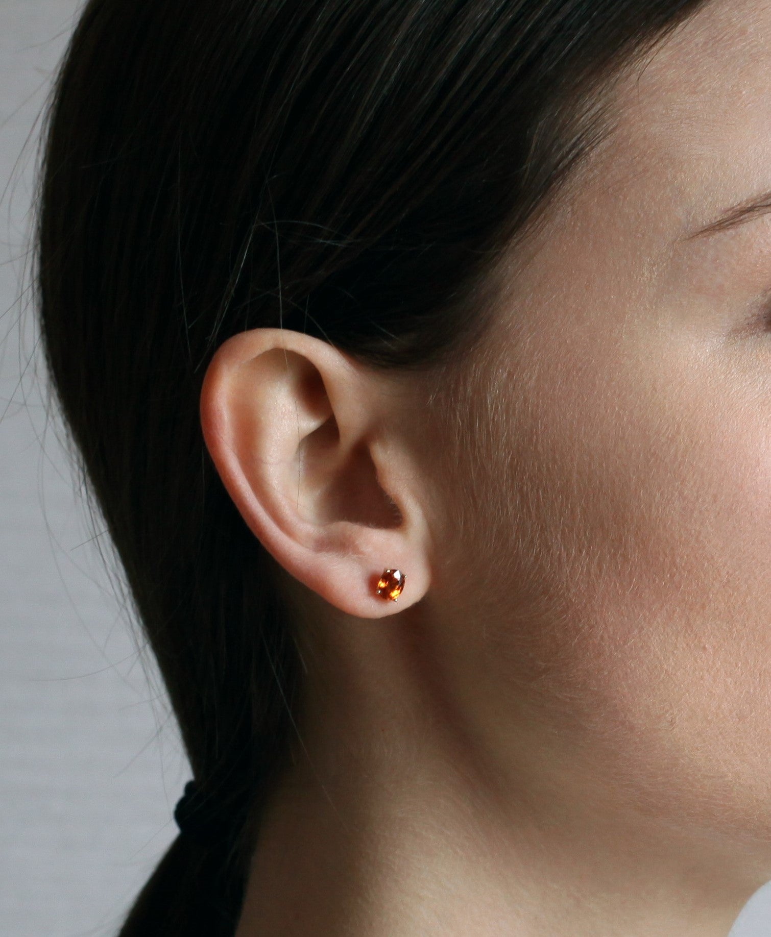 girl wearing orange garnet gemstone stud earrings spessartite garnet oval shape yellow gold fine jewelry montreal jewelry designer small color gemstone simple minimalist jewelry designer montreal color gemstone bridal jewelry specialist