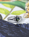 A contemporary white gold ring with a teal sapphire, set against a colorful scene to enhance its uniqueness and refined craftsmanship.