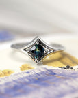 The Adorn ring in a soft-hued setting, highlighting the cushion-cut teal sapphire’s vibrant tones and its polished white gold band.