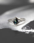 The Adorn ring glows against a dark backdrop, emphasizing its deep teal sapphire and bold white gold setting. A striking piece by Bena Jewelry.
