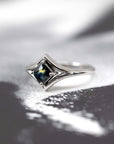 Dramatic lighting highlights the cushion-cut teal sapphire, enhancing the edgy elegance of this custom white gold ring. Handmade in Montreal.