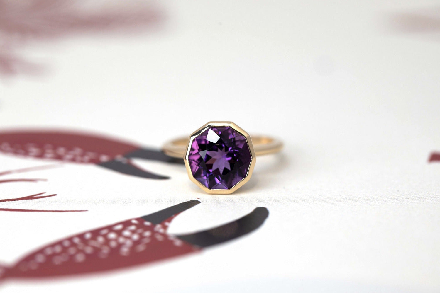 Bijou Round Amethyst Ring with pink undertones, handcrafted by Bena Jewelry à Montreal, showcased on a bold red and white surface.