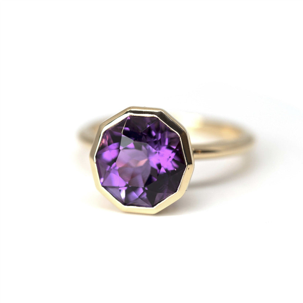 Close up of a bold yellow gold ring featuring a deep violet round amethyst, created by Canadian designer Bena Jewelry, captured on a white backdrop.