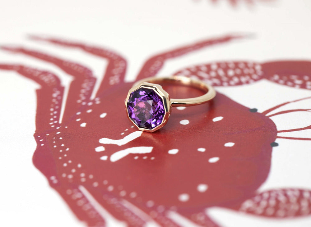 Yellow gold Round Amethyst Ring with a bold design, showing side view of the jewellery glowing against a white and red backdrop, crafted by Bena Jewelry à Montreal.