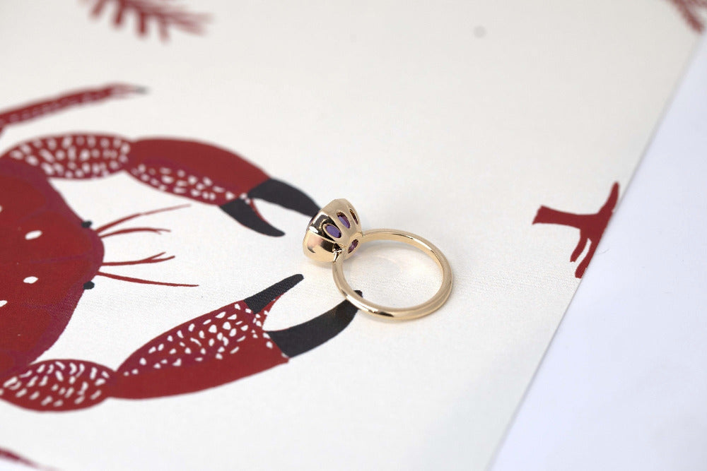 Back view of Bijou Round Amethyst Ring with a natural violet gemstone, bezel-set in yellow gold, displayed on a vibrant white and red background.