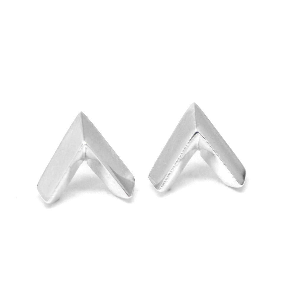 Collection of white gold arrow-shaped studs on a plain white background. Featuring a minimalist and statement-worthy design, these unisex earrings are handcrafted by Bena Jewelry in Montreal.