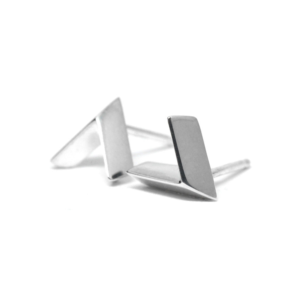 Close-up of a white gold arrow-shaped stud on a white background, minimalist, unisex, edgy, and bold design made in Montreal by Bena Jewelry, a Canadian fine jewelry designer.