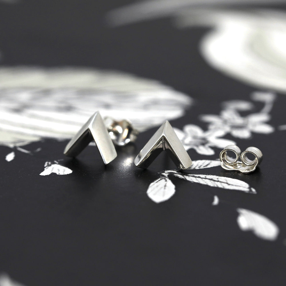 Pair of Arrow studs in white gold set against a deep, shadowy backdrop. A bold and contemporary unisex design created by Bena Jewelry, a Canadian fine jewelry designer in Montreal.
