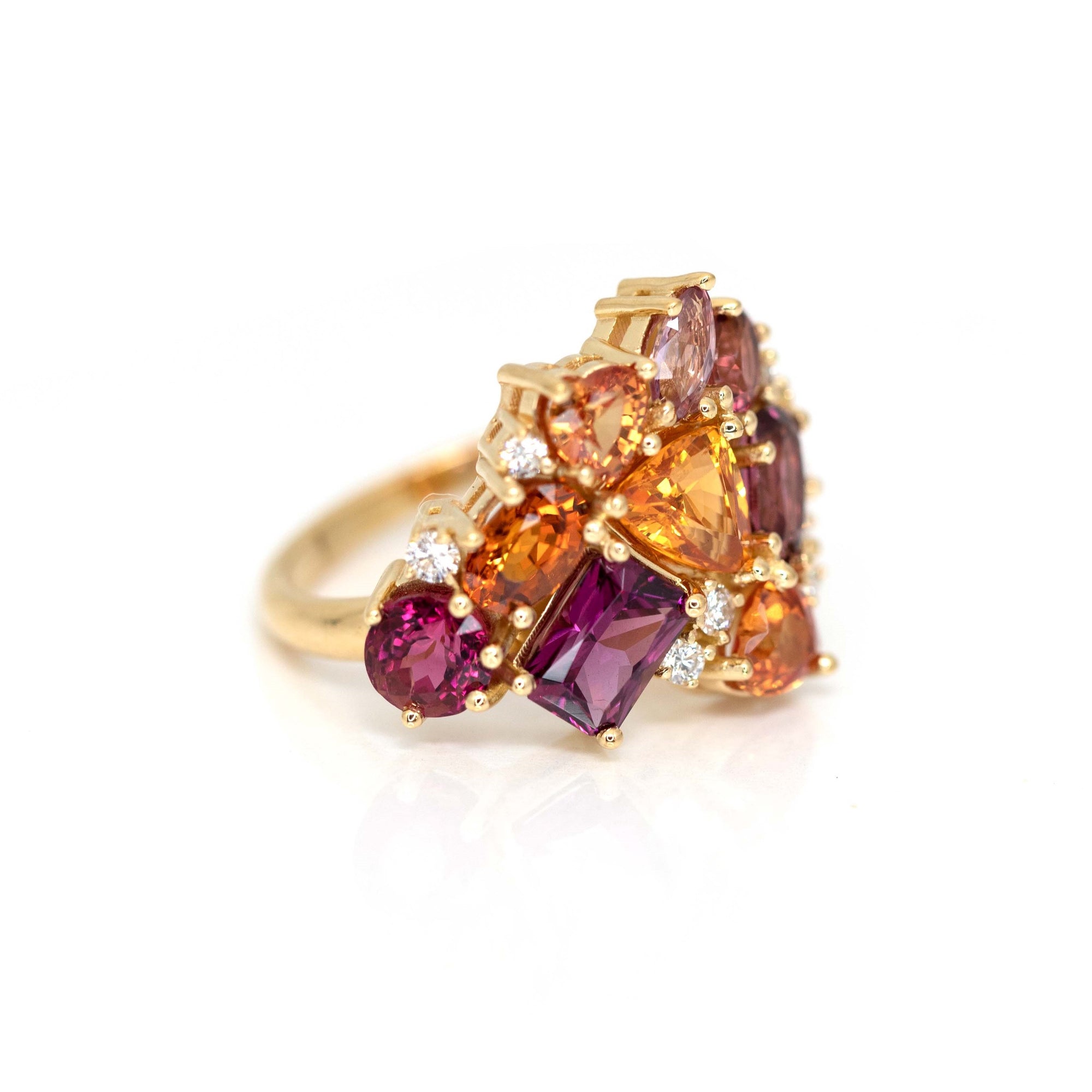 Close-up: Focuses on the variety of gemstone cuts, including trillion, heart, and emerald shapes, and their vivid orange, red, and purple hues. Made by Bena Jewelry, Montreal, Canada.