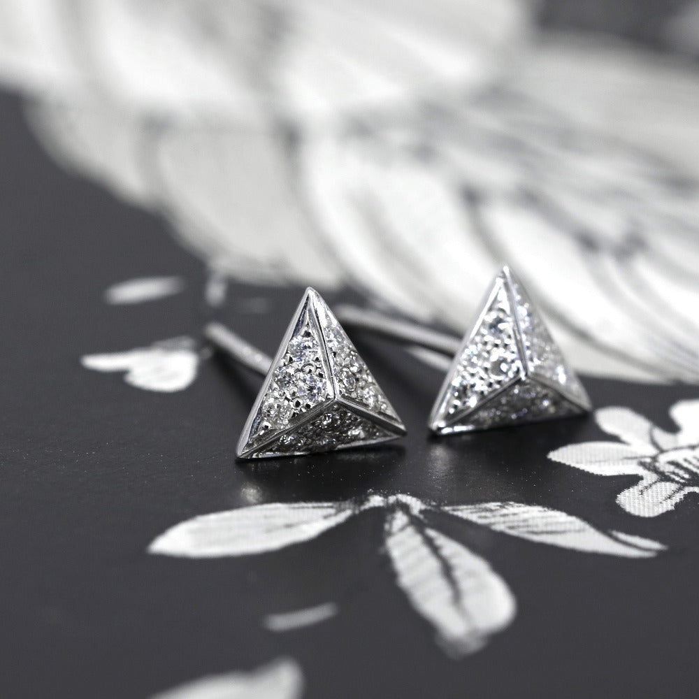 Angled close-up of one earring highlighting the sharp pyramid lines, reflective white gold surface, and sparkling diamonds.