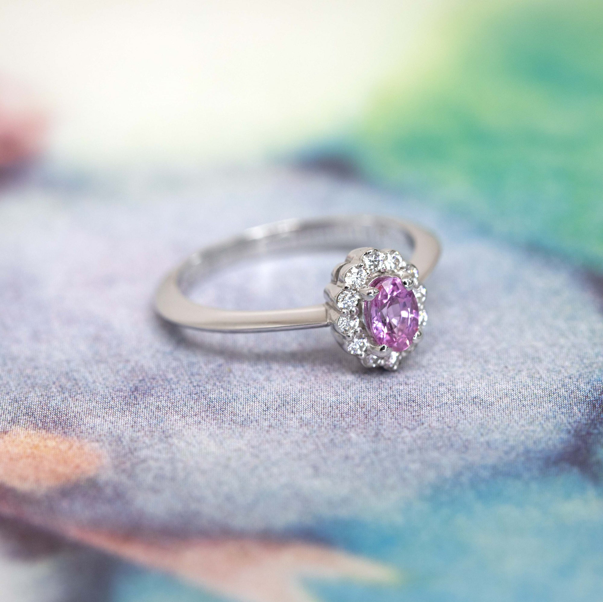 Oval pink sapphire engagement ring with a diamond halo, crafted in white gold by Bena Jewelry, highlighting fine craftsmanship and timeless beauty.