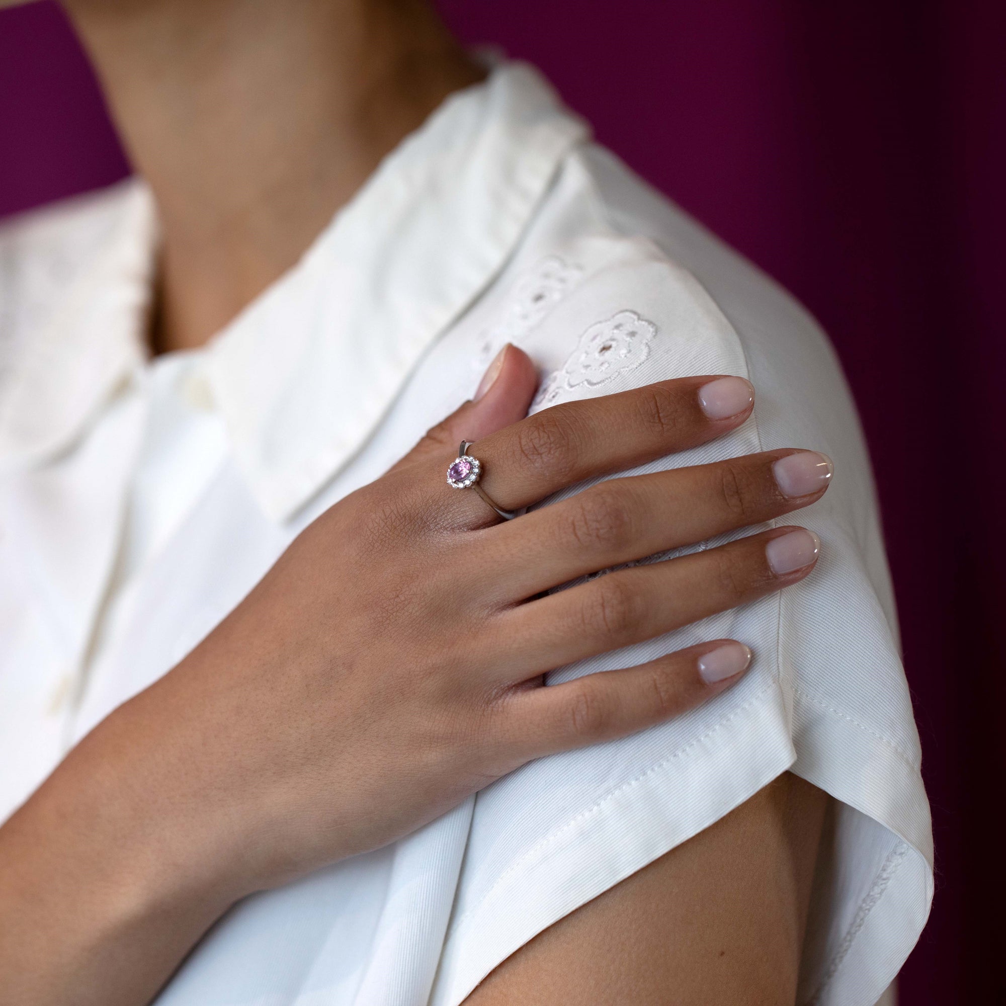 Close-up of a woman’s hand wearing the Diamond Halo Pink Sapphire Ring in white gold, showcasing the vibrant pink sapphire and delicate diamond halo, handcrafted by Bena Jewelry.