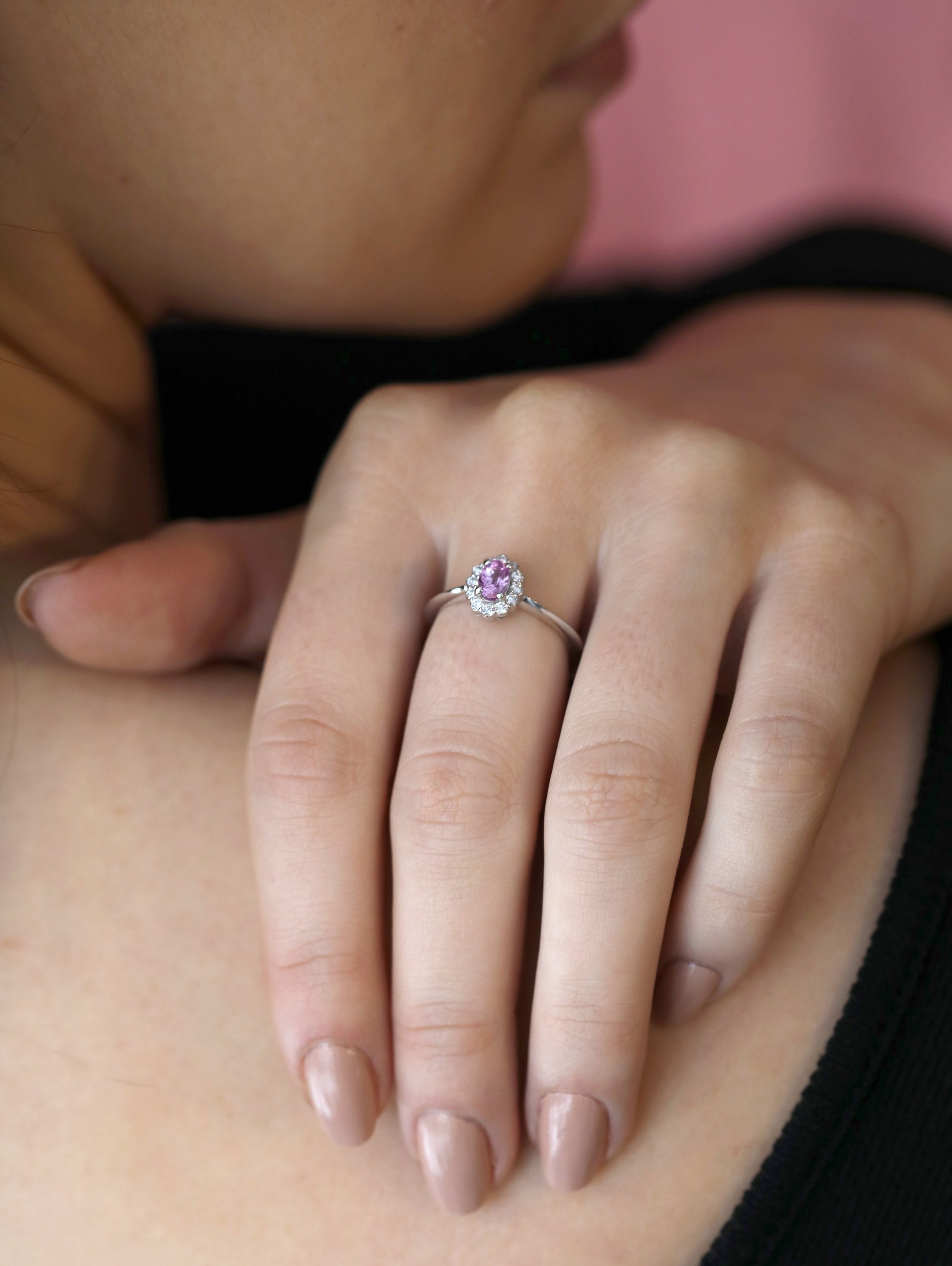 Elegant bridal ring with a pink sapphire and diamond halo, worn on a woman’s hand, highlighting its white gold band, custom-designed by Bena Jewelry in Canada.