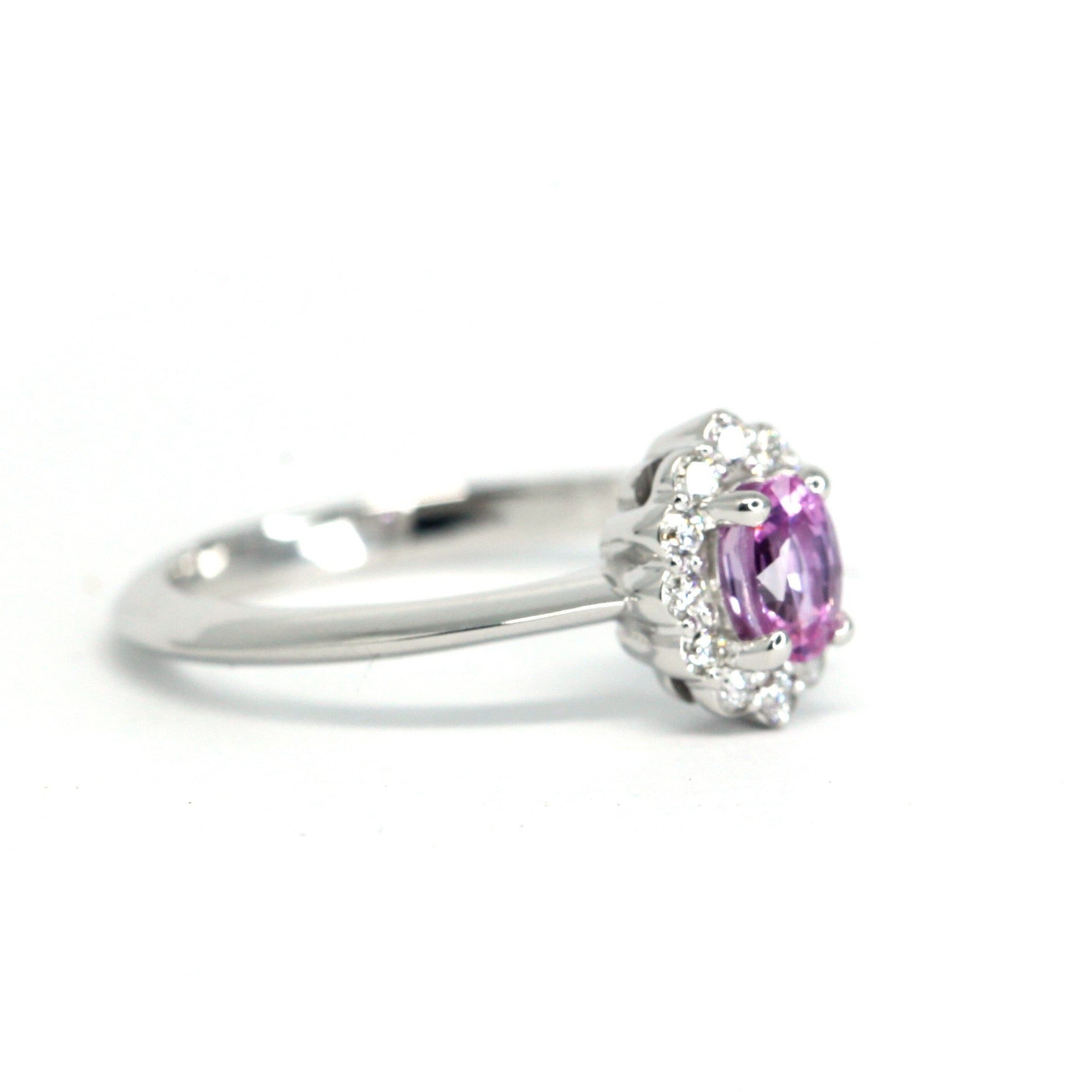 Side view of an elegant white gold engagement ring with a diamond halo and vibrant pink sapphire, handcrafted by Bena Jewelry, displayed on a clean white background.