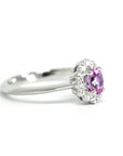 Side view of an elegant white gold engagement ring with a diamond halo and vibrant pink sapphire, handcrafted by Bena Jewelry, displayed on a clean white background.