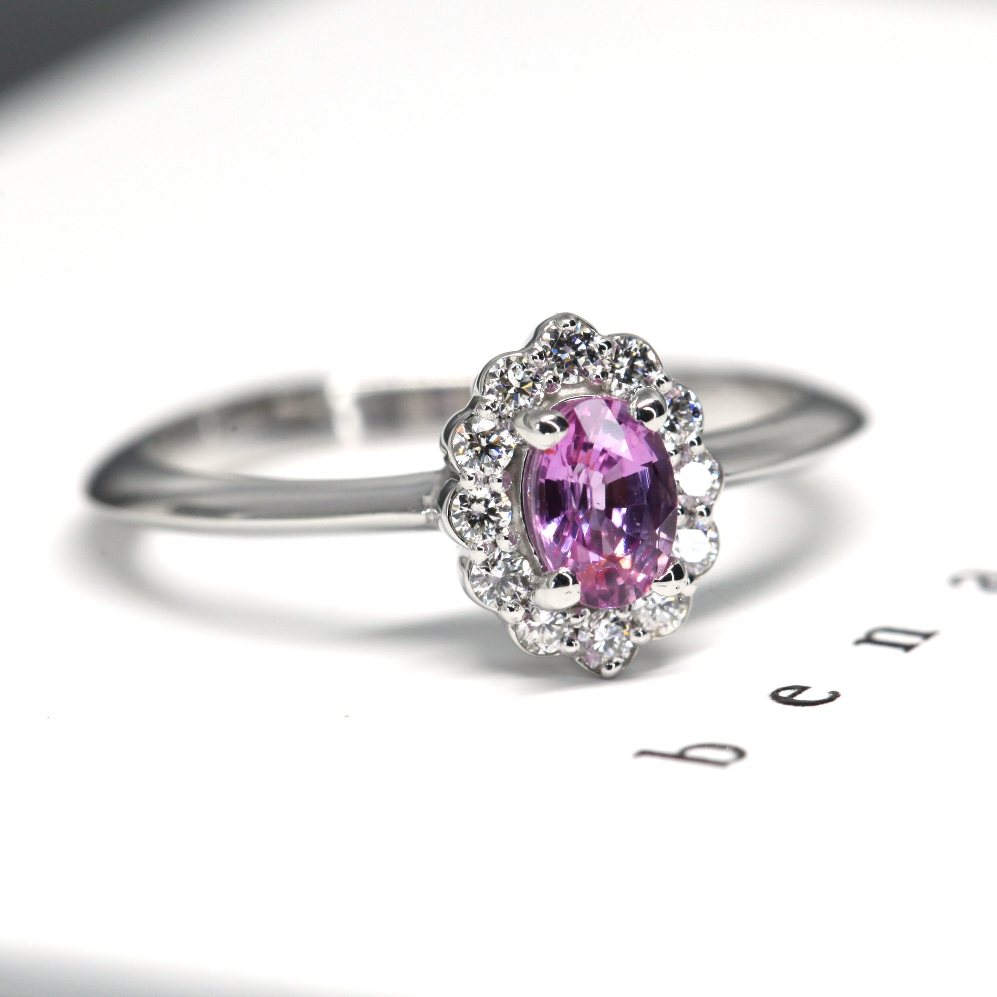 White gold engagement ring by Bena Jewelry featuring an oval pink sapphire and a diamond halo, custom-made in Montreal with natural gemstones.