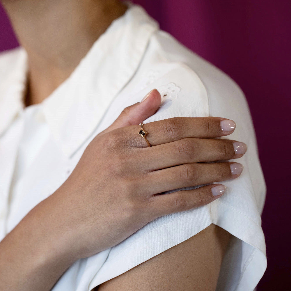 Kink Baguette Chocolat Diamond Ring in yellow gold with a twisted band and baguette-cut chocolate diamond by Bena Jewelry, shown in a close-up on a woman’s hand.