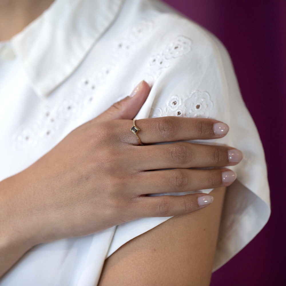 Yellow gold Kink Baguette Chocolat Diamond Ring by Bena Jewelry, showcasing a modern twisted band and a baguette-cut brown diamond in a close-up on a woman’s hand.