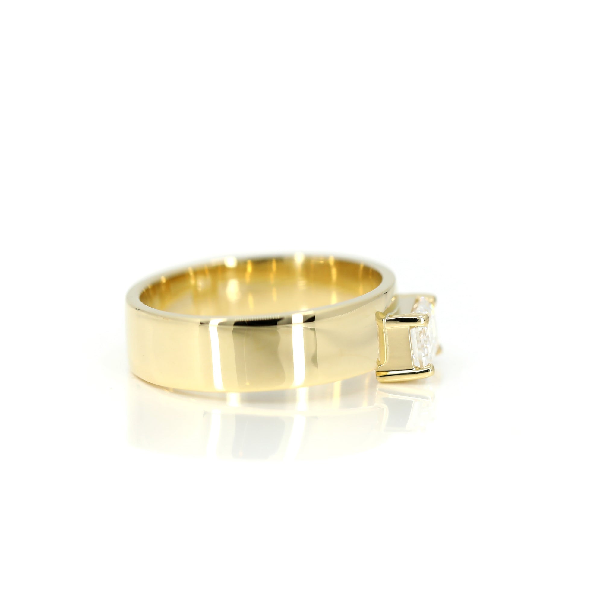Close-up of a yellow gold engagement ring featuring an emerald-cut diamond. A sleek and contemporary creation by Bena Jewelry, handcrafted in Montreal.