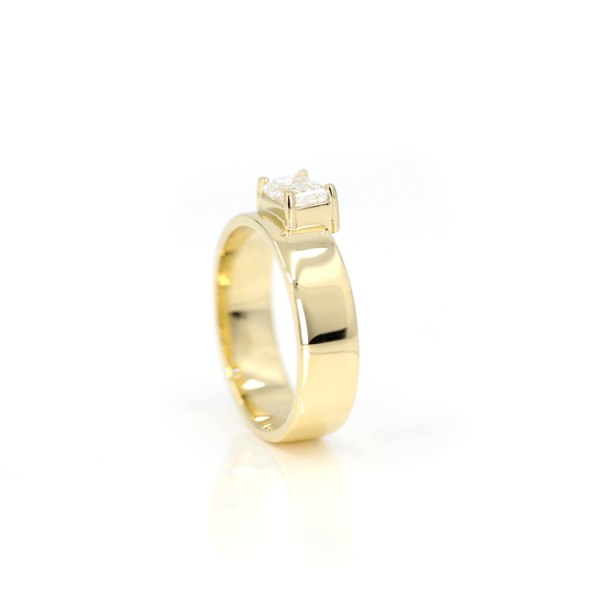 Close-up of a contemporary yellow gold engagement ring with an emerald-cut diamond. Designed and crafted in Montreal by Canadian jeweler Bena Jewelry.
