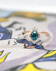 front view of custom made montana blue green sapphire diamond halo rose gold ring made in montreal on multi color background