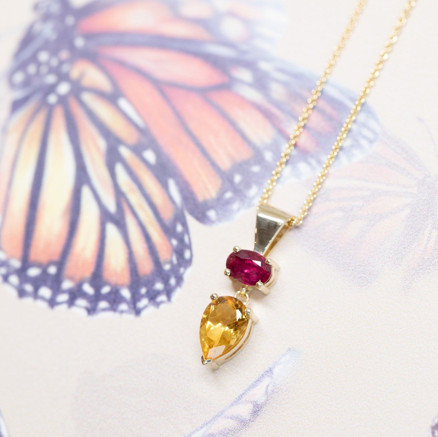 side view of pear citrine and ruby pendant made in yellow gold in montreal by bena jewelry designer on a multi color background