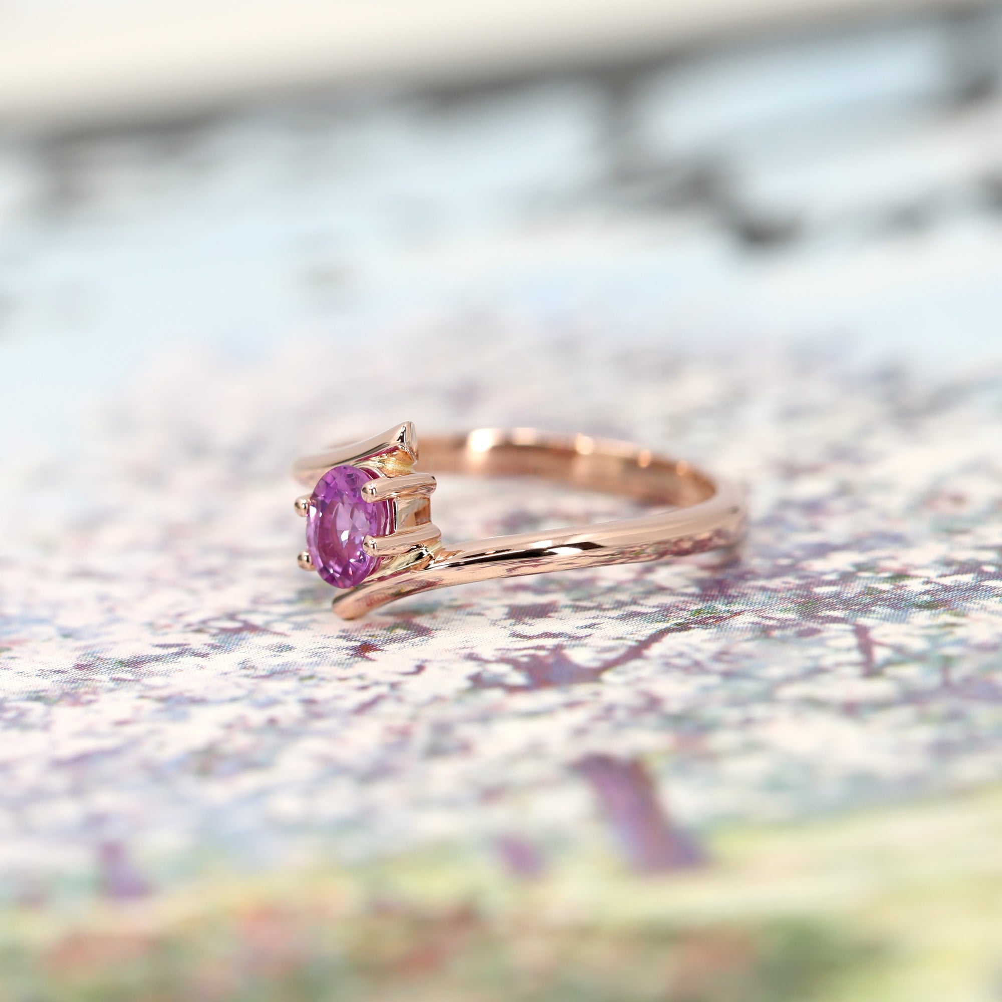 side view of bena jewelry kink ring made in montreal in rose gold with pink sapphire natural gemstone on multi color background