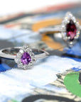 The Aura ring displayed against a soft-hued backdrop, enhancing the vibrancy of its pink-violet sapphire and diamond halo.