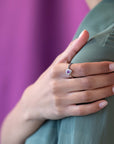 Close-up of the Aura engagement ring on the finger, showcasing the radiant pink-violet sapphire and brilliant diamond halo.