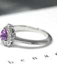 Custom-made bridal ring in white gold, featuring a mesmerizing pink-violet sapphire and diamond halo. Crafted by Bena Jewelry.
