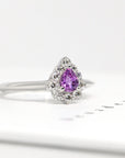Close-up of the Aura ring, highlighting its pear-shaped pink-violet sapphire and surrounding diamond halo. A timeless engagement piece in white gold, crafted by Bena Jewelry in Montreal, Canada.