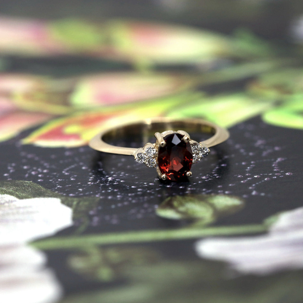 Yellow gold Désir Pyrope Garnet Ring with an oval garnet centerpiece and side diamonds by Bena Jewelry displayed on a soft pastel background custom bridal ring Montreal