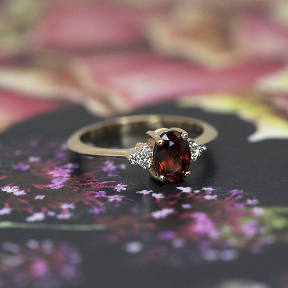 Désir Pyrope Garnet Ring in yellow gold featuring an oval pyrope garnet and diamonds by Bena Jewelry displayed on a vibrant colored background custom-made in Montreal