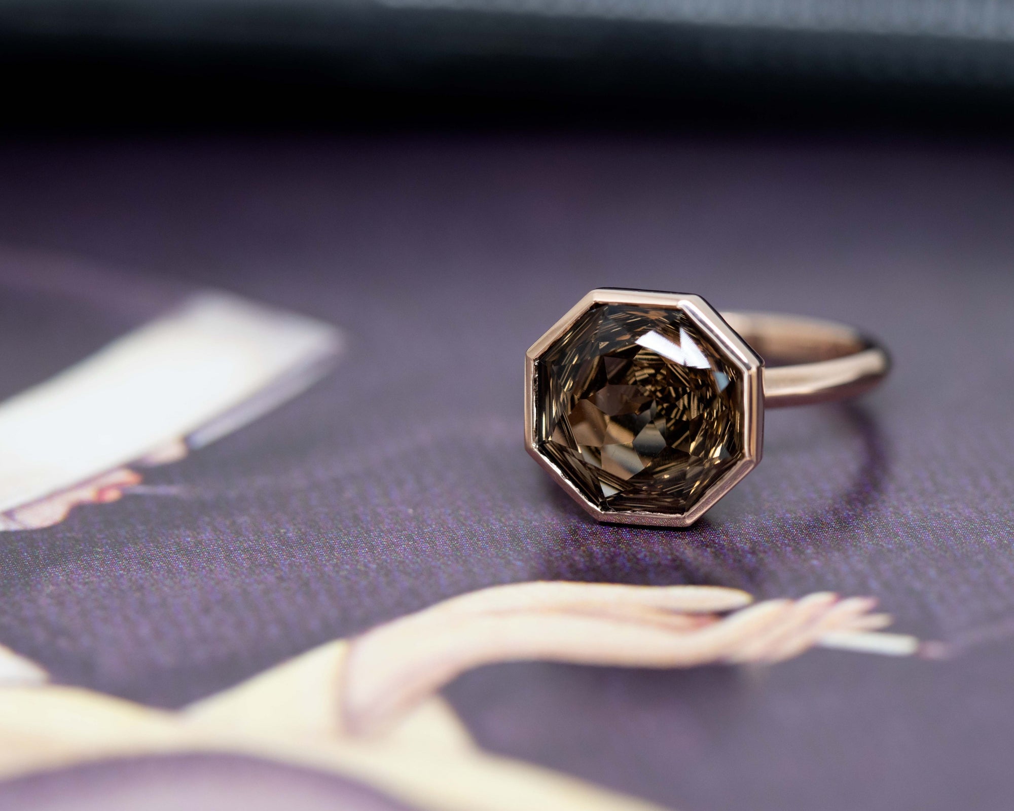 Rose gold cocktail ring with a Brazilian smoky quartz, featuring a round-octagon cut, displayed on a bold white and red background.