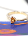 side view of trillion shape orange sapphire gemstone minimalist design custom made in montreal by the designer bena jewelry on a multi color background