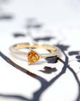 front view of a custom made minimalist bridal ring with a orange trillion shape sapphire made in montreal by bena jewelry designer on a black and white background