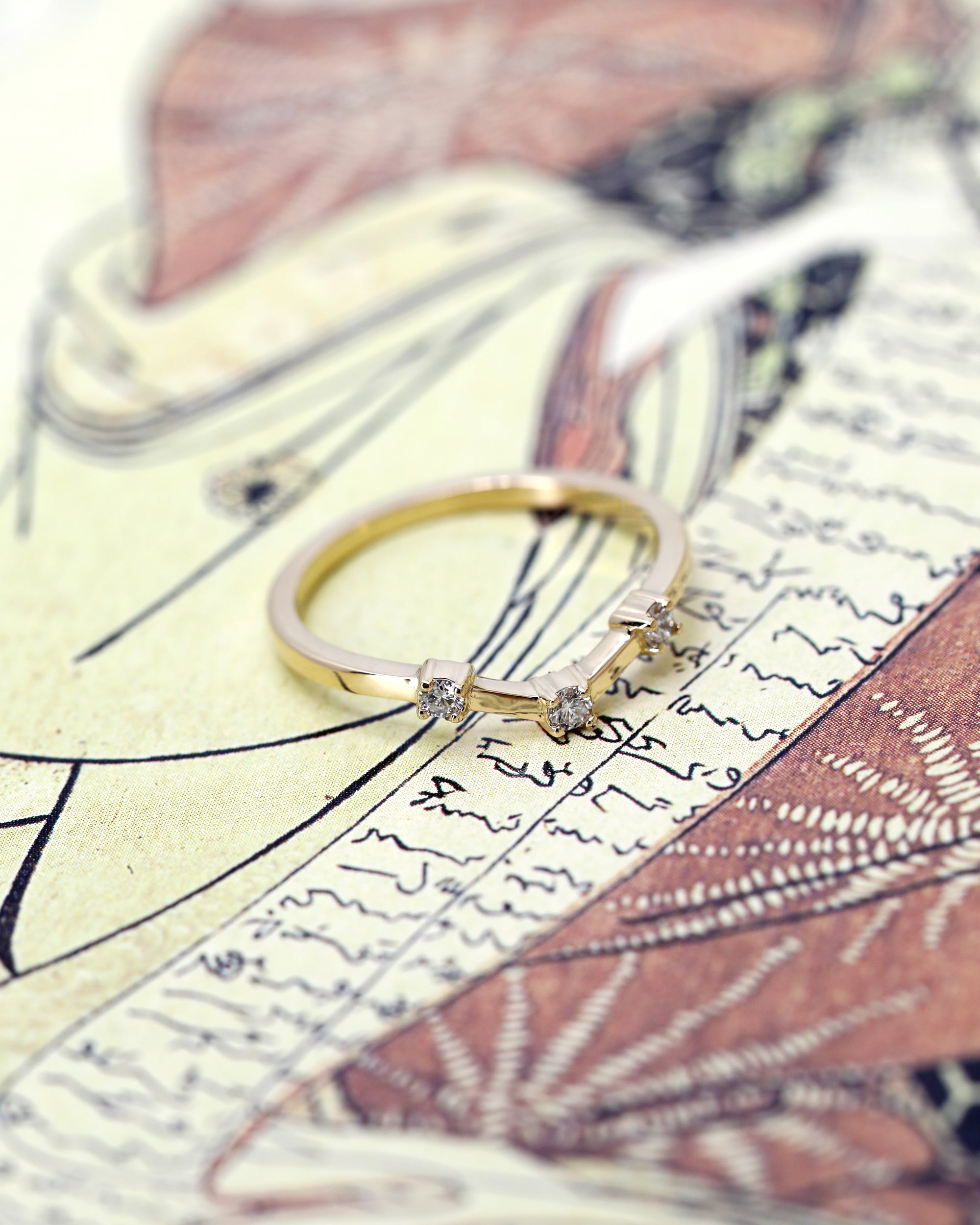 A unique yellow gold wedding band with round diamonds and a boxy style, displayed on a dramatic background. Modern fine jewelry by Canadian designer Bena Jewelry, Montreal.