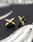 Yellow gold Cross Gold Studs with a voluminous geometric cross shape by Bena Jewelry, displayed on a black background, modern designer earrings made in Canada.