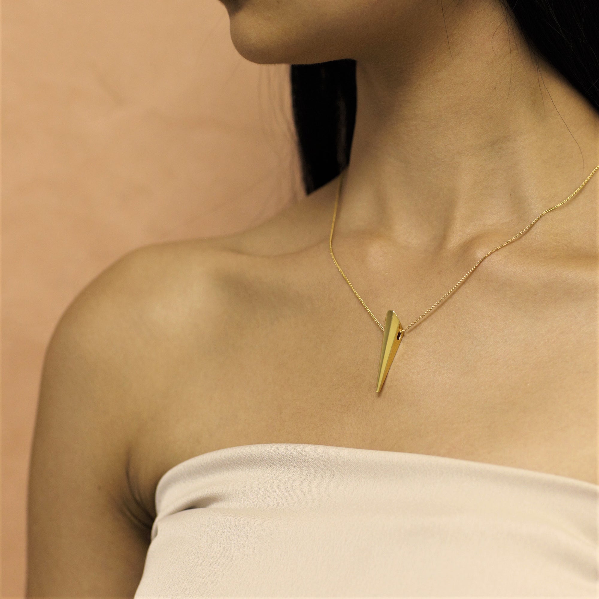 Close-up of Pike Pendant worn at the collarbone – A contemporary gold pendant adding a touch of power and refinement.