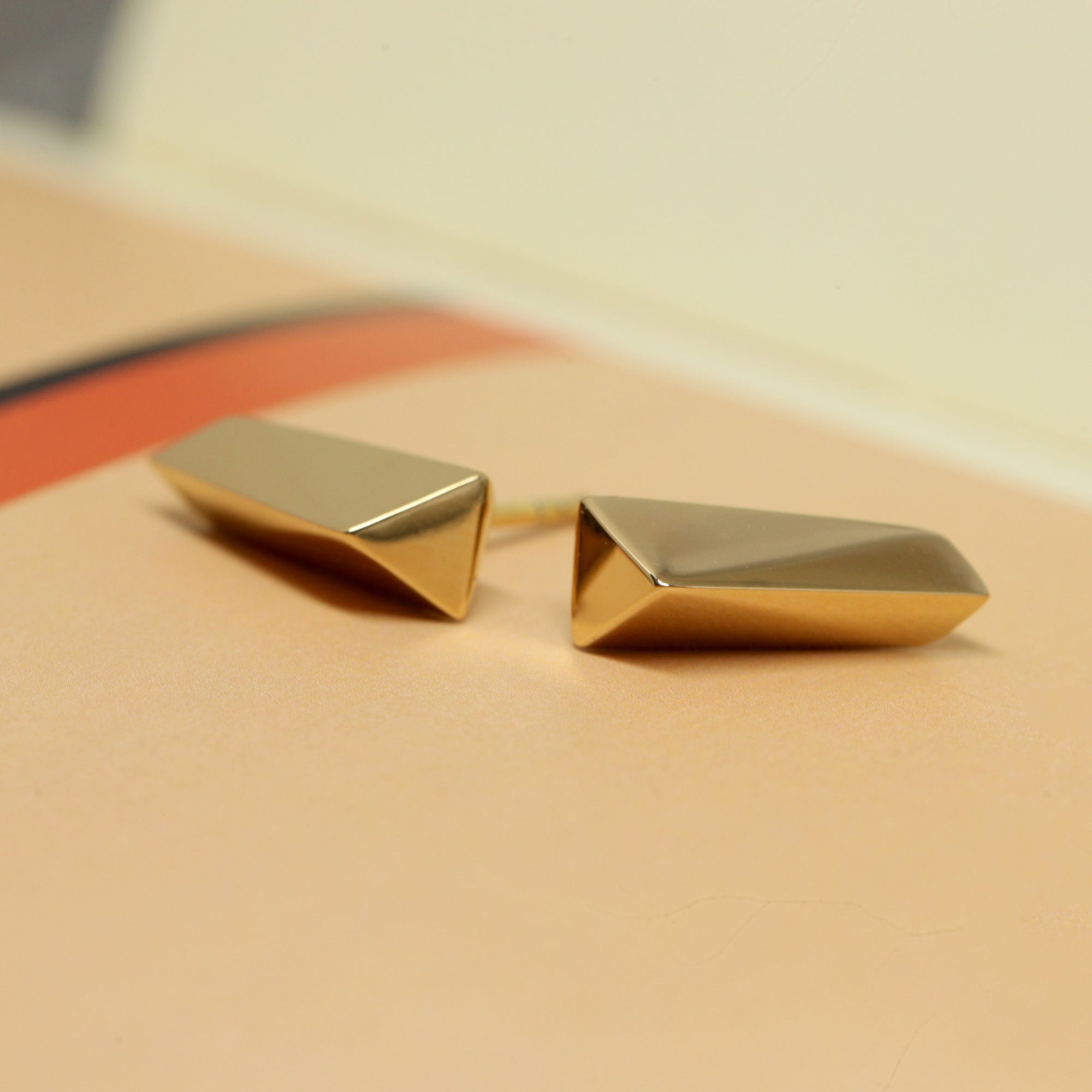 Close-up of gold earrings on dark background – The polished gold finish and bold edges stand out dramatically in this edgy fine jewelry design.