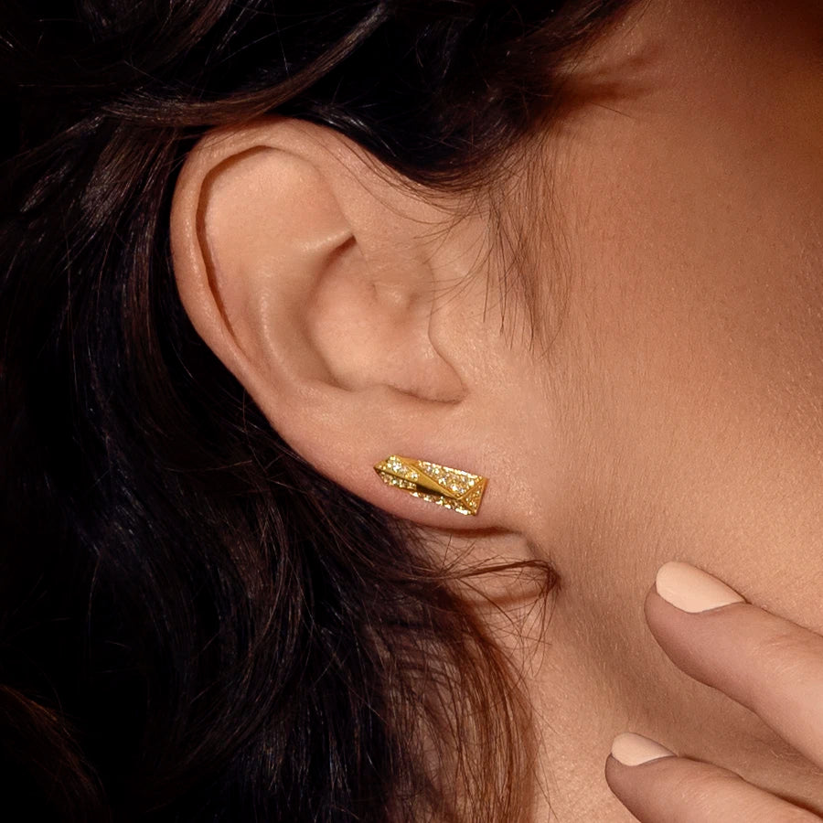 Close up on a woman&#39;s ear wearing a bold diamond stud earrings with geometric volumes. These edgy diamond studs were designed and crafted in Canada by high end brand Bena Jewelry.