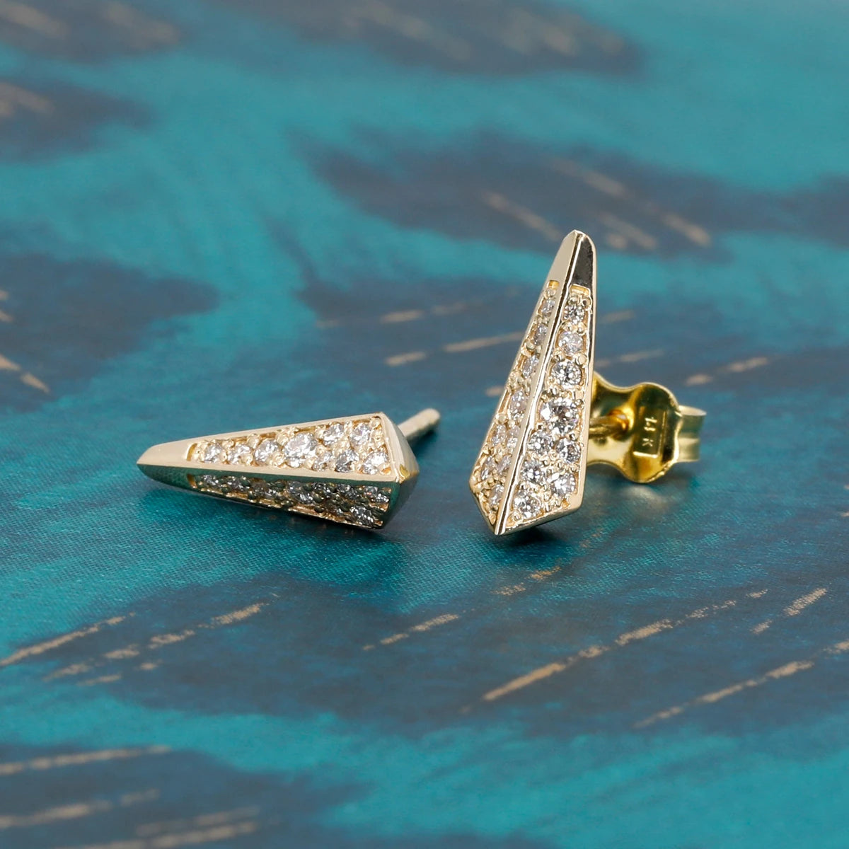 A pair of gold earrings with diamond pavé is photographed on a turquoise lepoard background. The earrings are gender-neutral and have a modern, elegant and chic style. Created by independent designer Bena Jewelry.